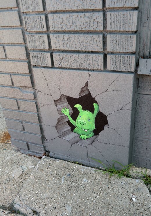 Green creature peeking through wall hole mural