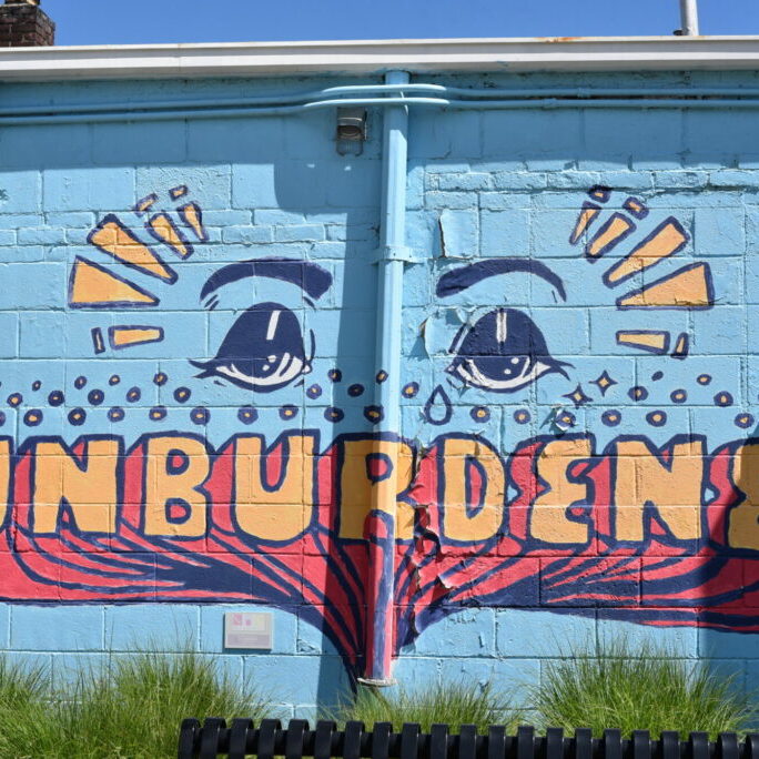 Colorful mural with eyes and word 'Unburdened'.