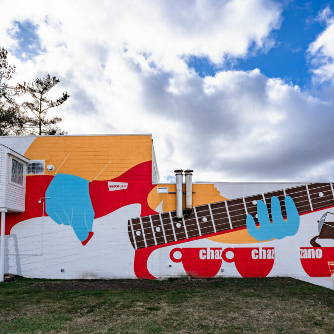 Colorful mural of guitar, cups, and hand on wall.