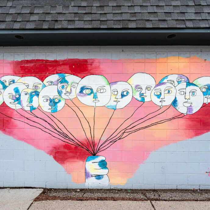 Colorful face balloons mural with hand on wall.