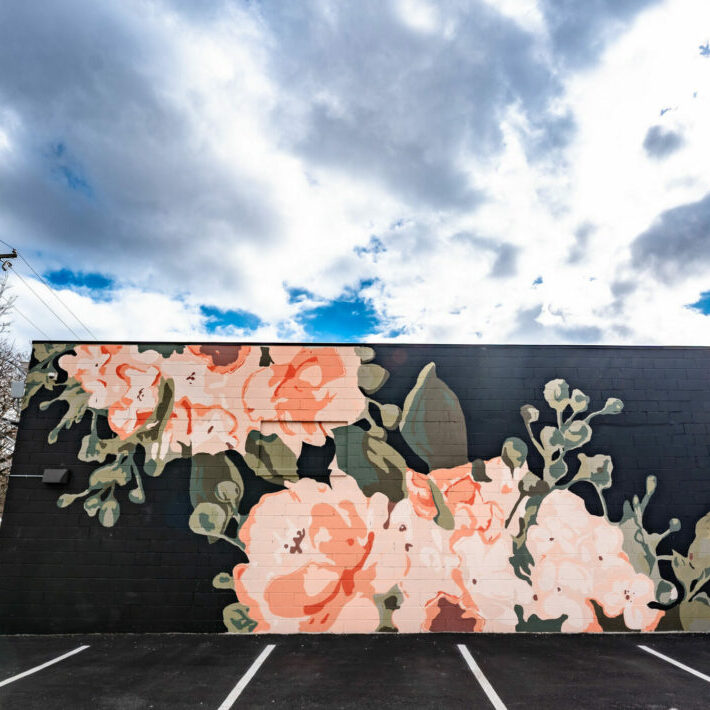 Floral mural on building wall under cloudy sky.